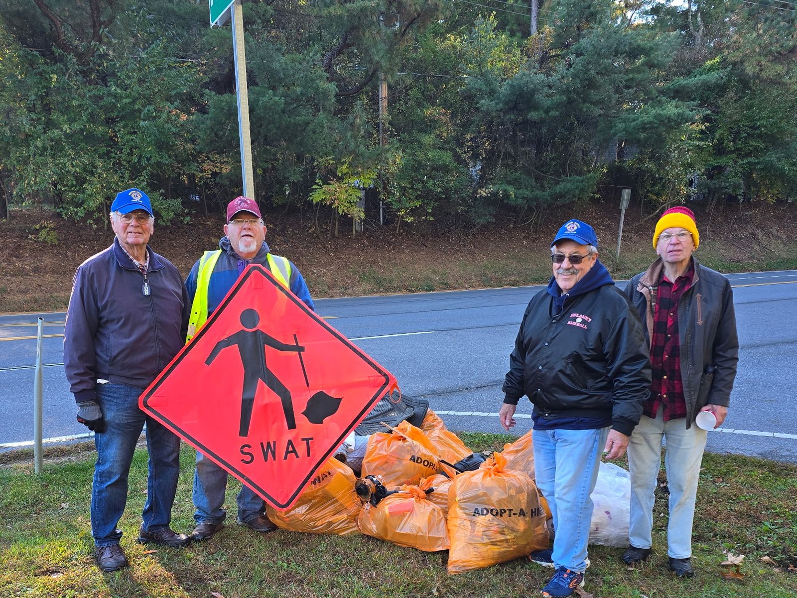 Four Freedom District Lions stand along Route 32 beside a pile of orange trash bags and an orange SWAT road sign after a road cleanup